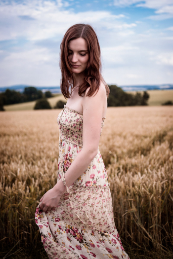 Girl in summer dress dances on a cornfield